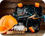 Orange construction helmet, work gloves, ear protection, and various tools on a wooden surface with a black toolbox.