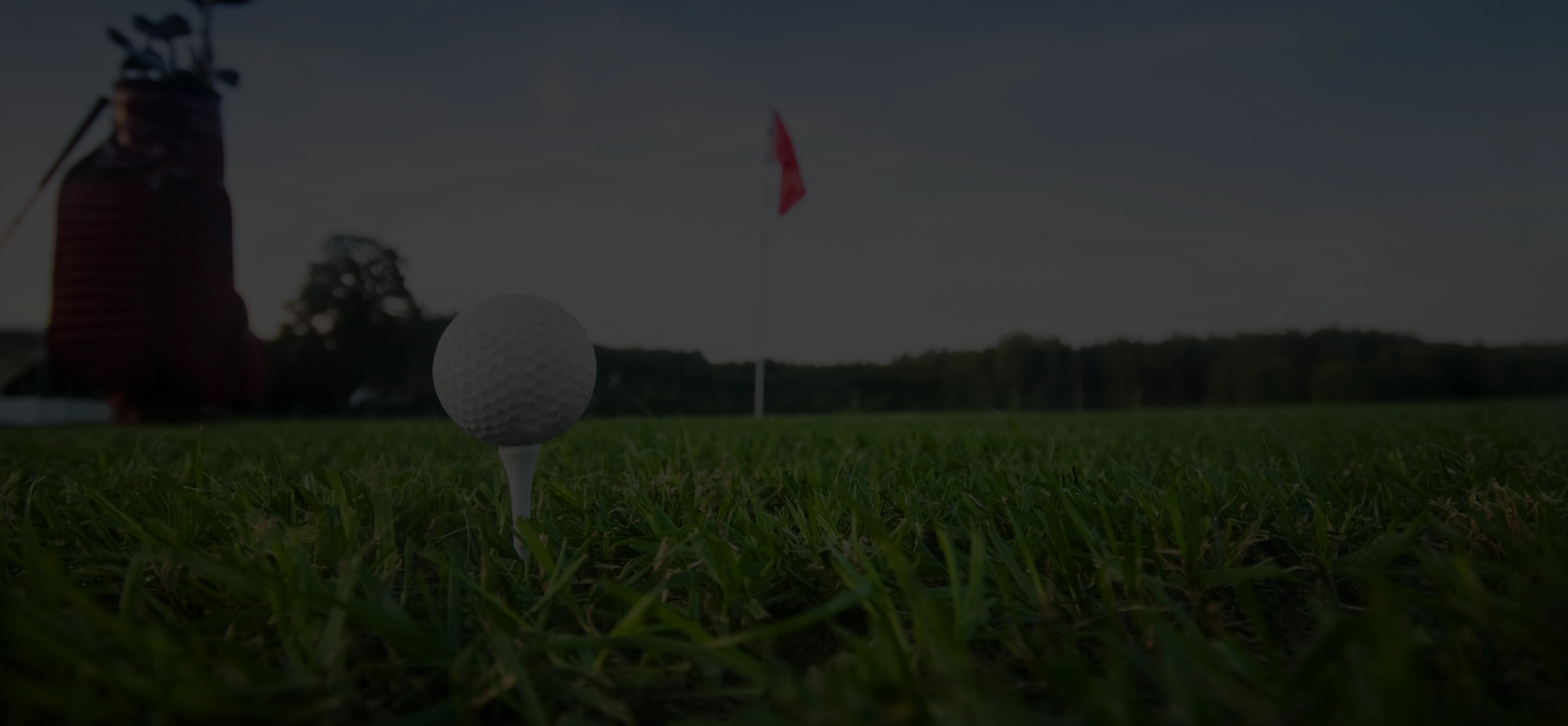 Close-up of a golf ball on a tee on green grass with a red flag and golf bag in the background.