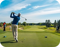 Golfer in blue shirt swinging a golf club on a green golf course under a blue sky.