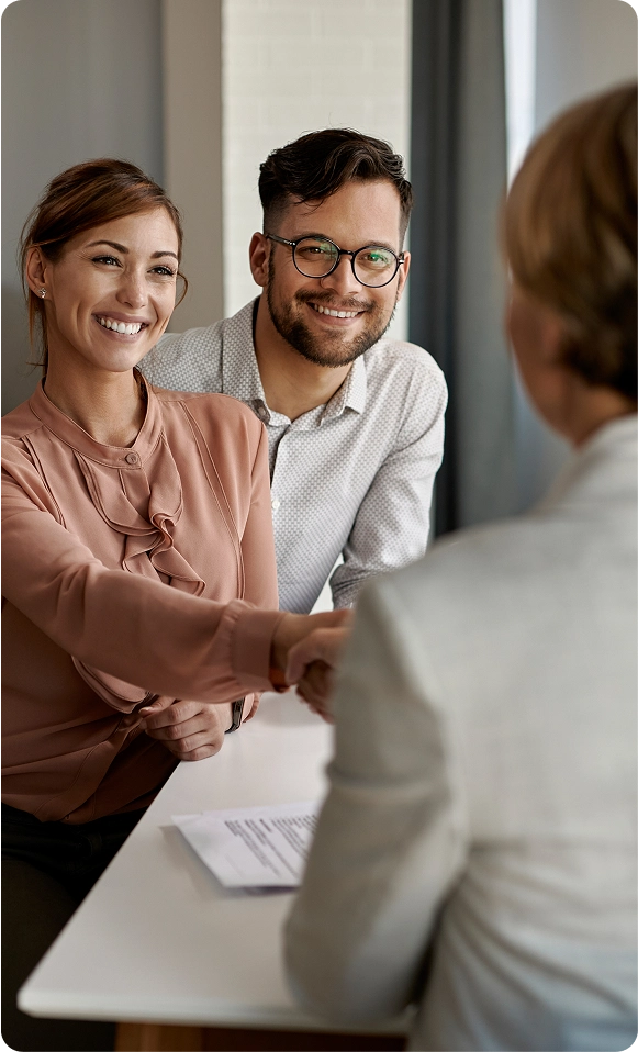 Smiling woman and man shaking hands with a person across a table during a meeting.