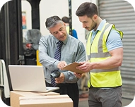 Two men reviewing documents together, one in business attire and the other wearing a safety vest on a construction site.