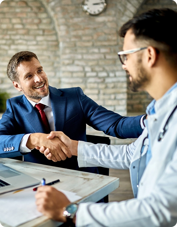 Businessman smiling and shaking hands with a doctor in a medical office.