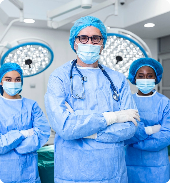 Three medical professionals wearing surgical scrubs, masks, and caps in an operating room with surgical lights in the background.