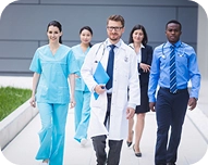 Group of allied health professionals walking outside, including doctors, nurses, and a professional in a blue shirt and tie.