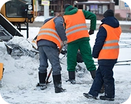 Three workers in orange safety vests shoveling snow on a street.