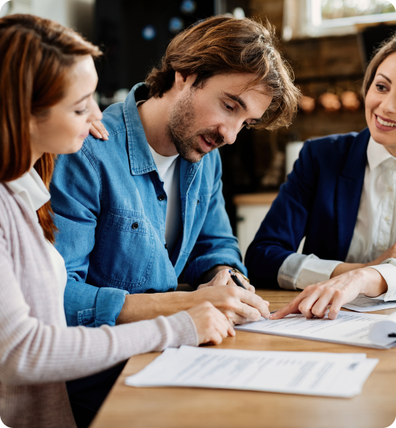 Young couple signing a document at a table with a professional woman pointing at the paper.