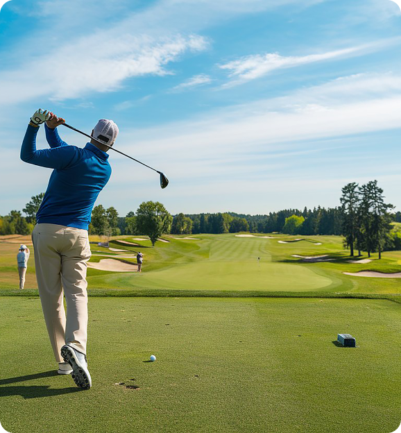 Golfer in blue shirt and beige pants swinging a golf club on a sunny golf course with a clear blue sky.