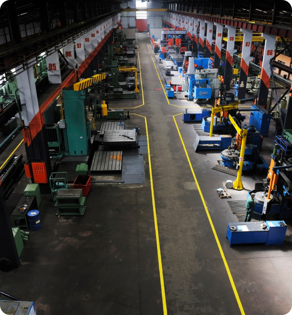 Spacious industrial factory floor with machinery and equipment lined up on both sides of a yellow-marked central aisle.
