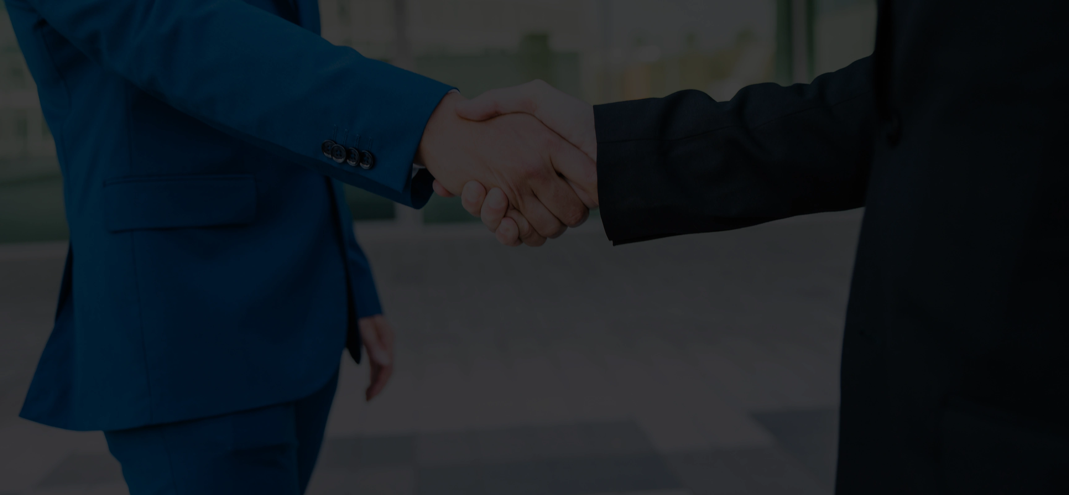 Two people in business suits shaking hands in an outdoor urban setting.