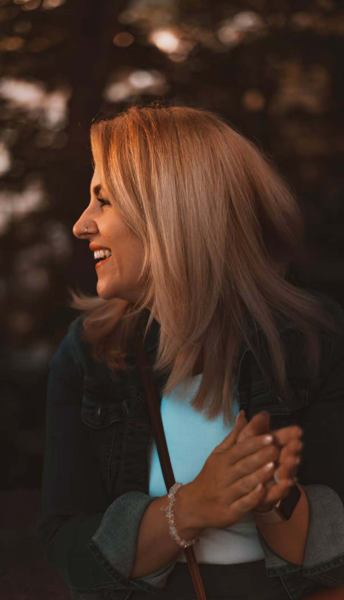 Smiling woman with blonde hair clapping hands outdoors in soft warm light.