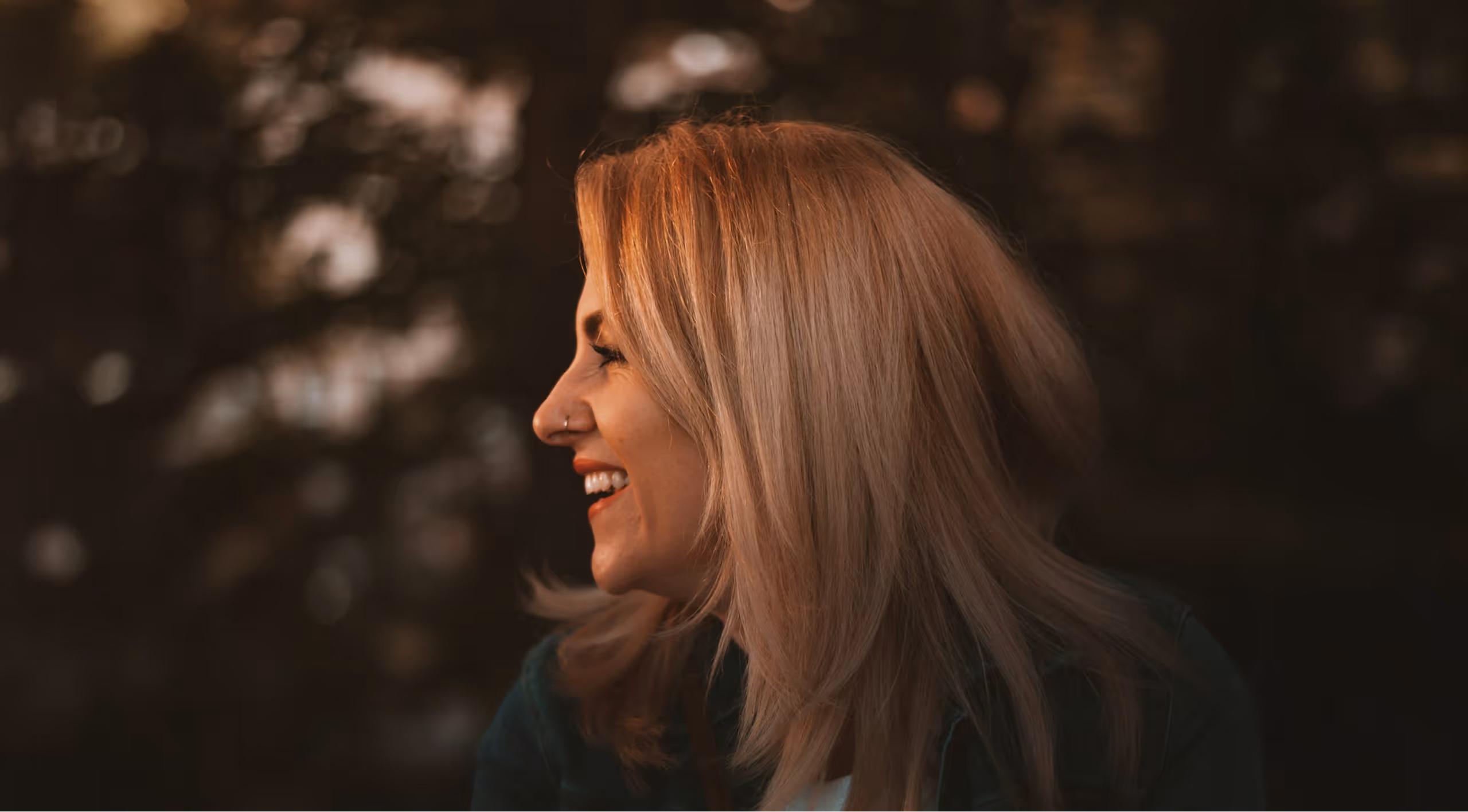 head of a blond woman looking to her right, her face is lit by the setting sun