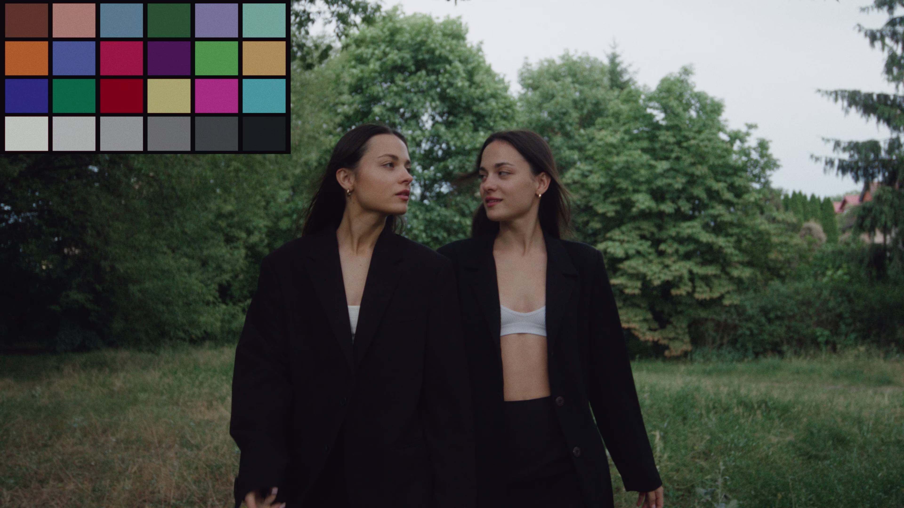 Two women with long dark hair wearing black blazers and white tops standing outdoors in front of trees.