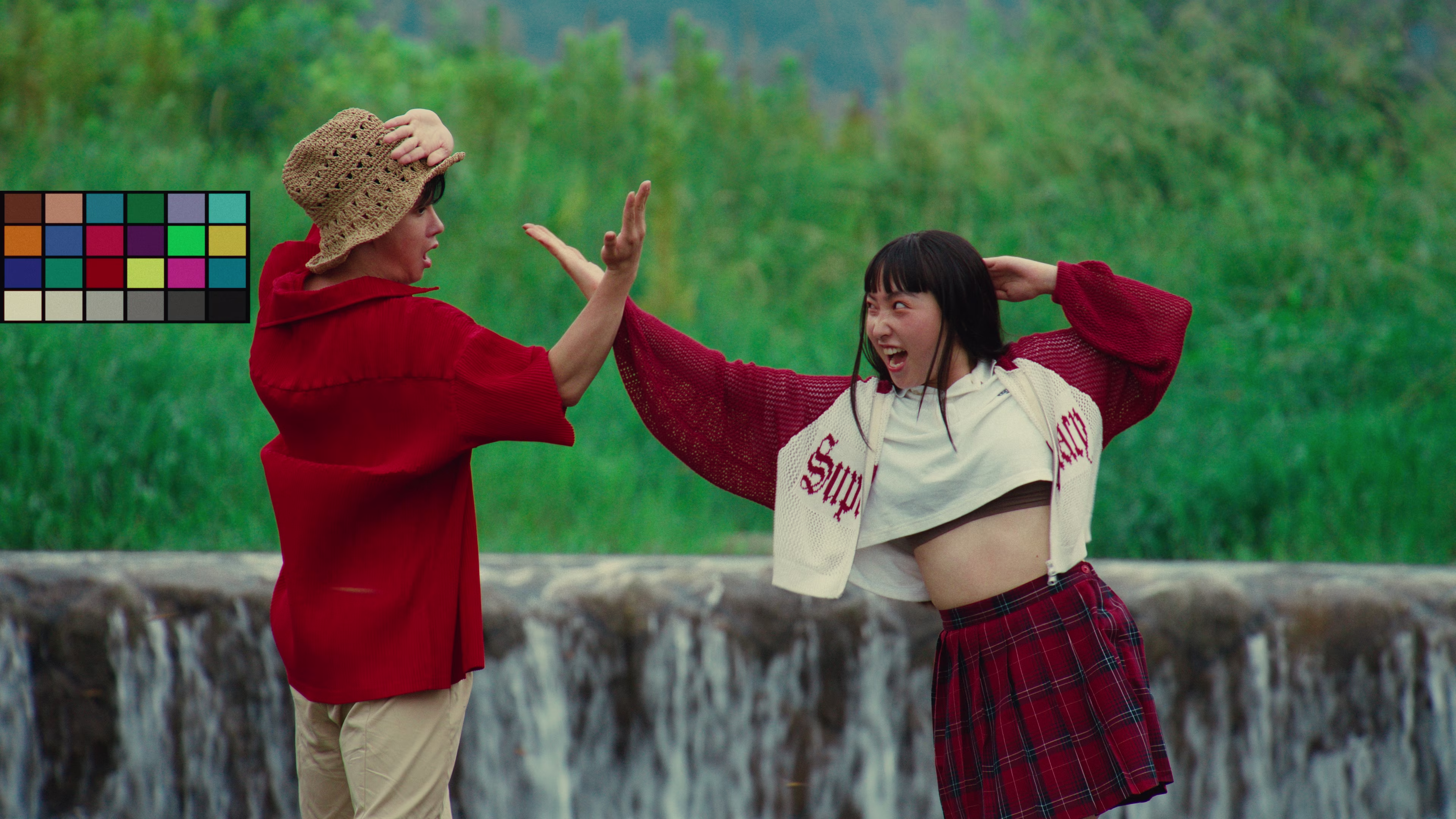 Two young people playfully interacting outdoors near a small waterfall with lush green background.