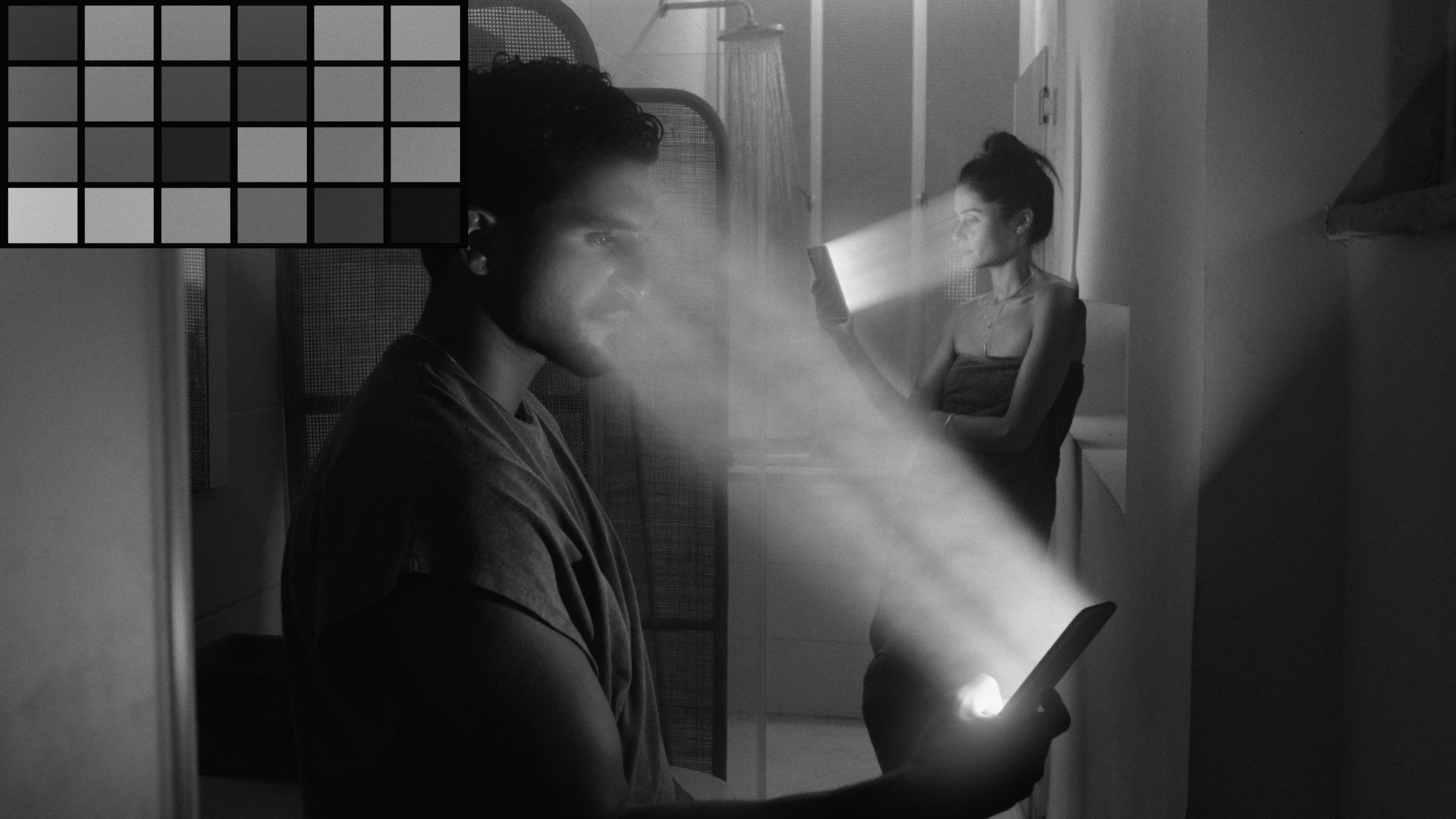 Black and white photo of a man and woman each holding smartphones projecting beams of light from their screens in a dimly lit room.