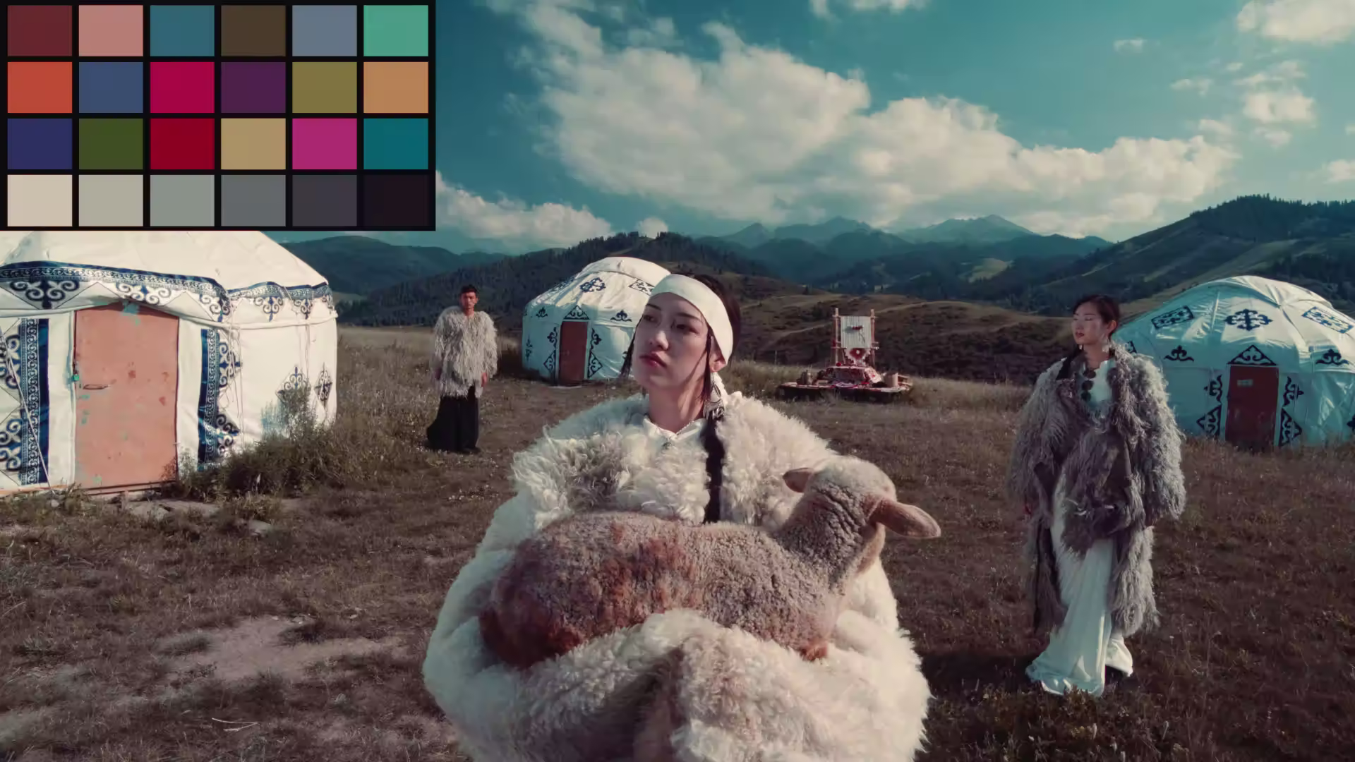 Three people in traditional fur clothing near yurts in a mountainous landscape, one holding a lamb.