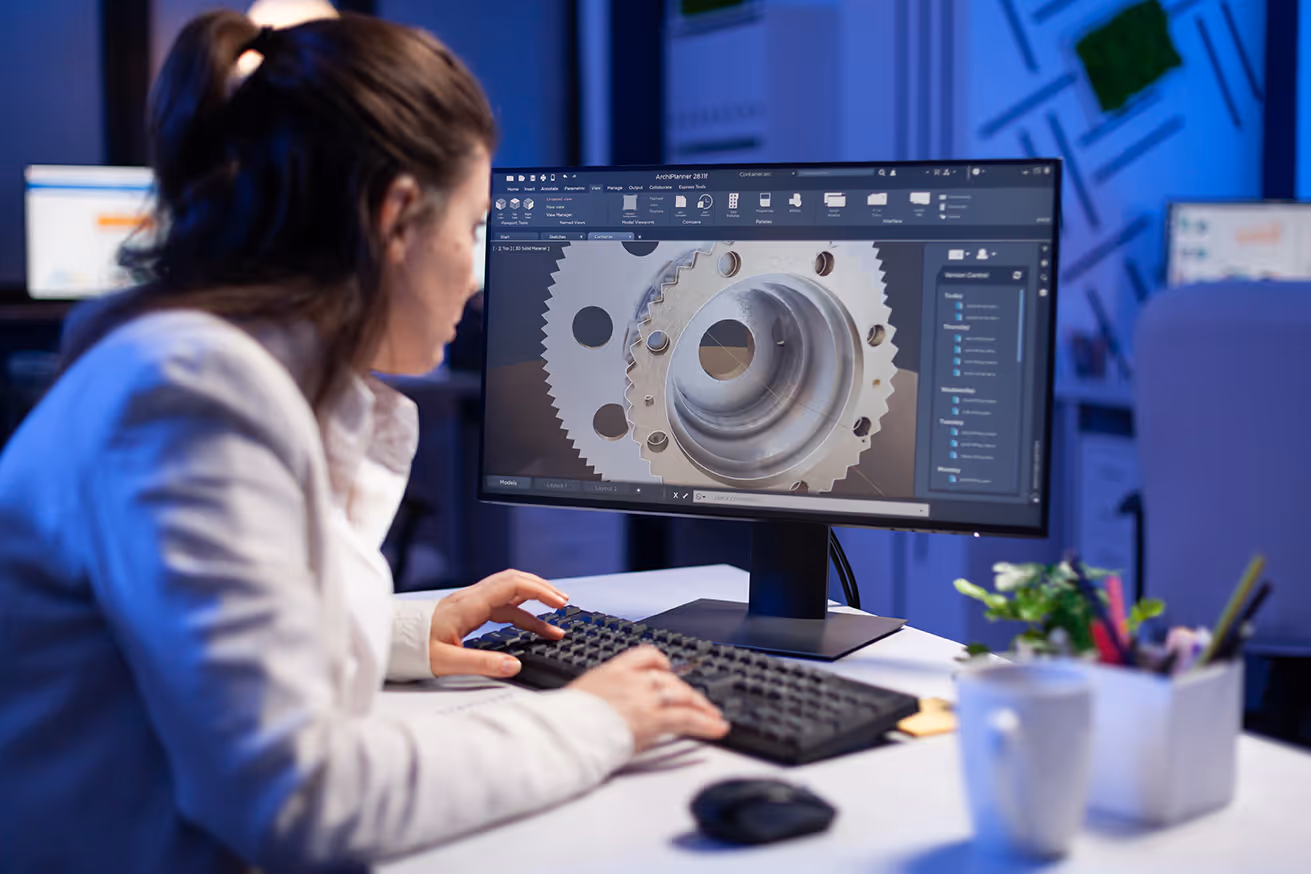 Woman working on a computer with 3D modeling software displaying a mechanical gear design.