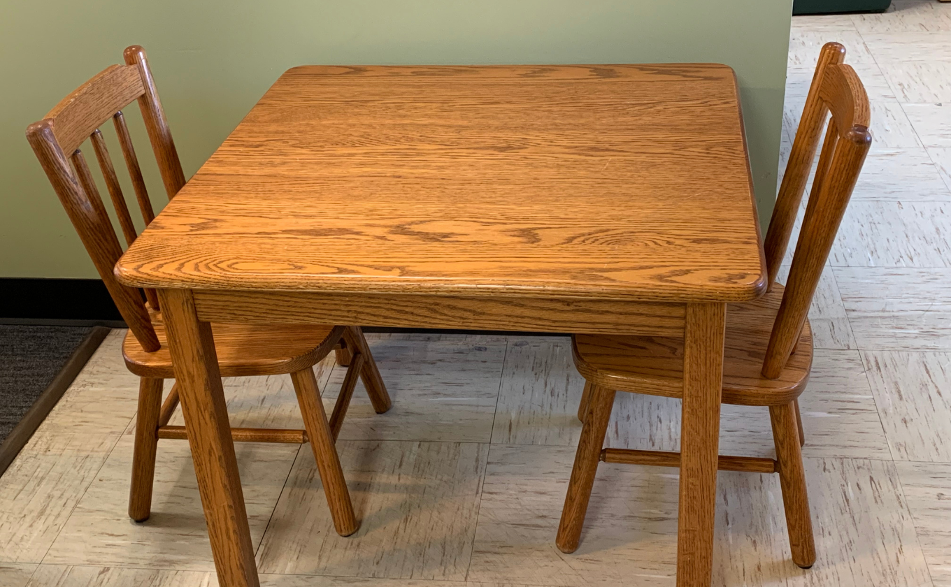 Small oak wood table with two matching chairs on light tile floor near green wall.