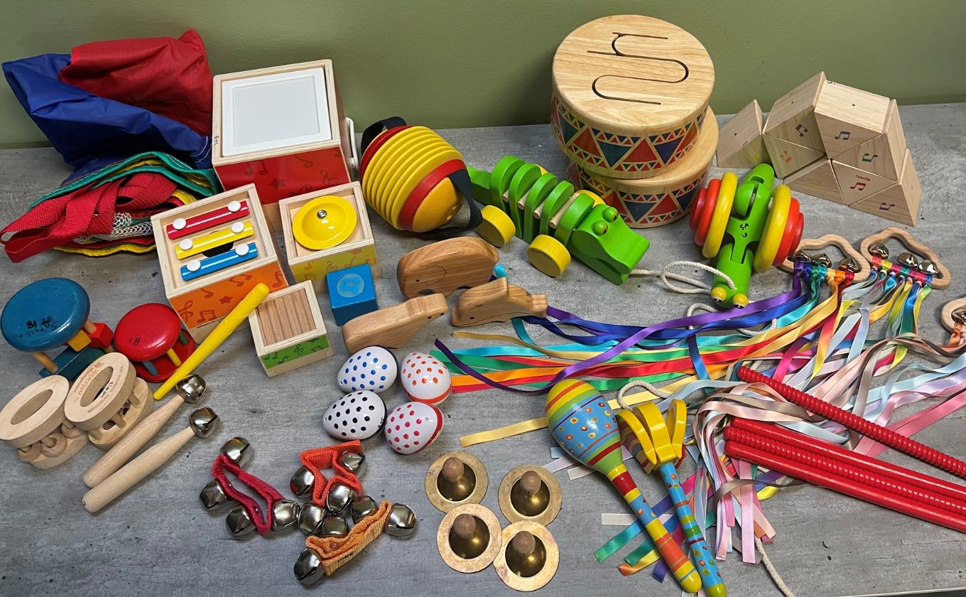 Assorted colorful wooden musical instruments and rhythm toys on a table including maracas, tambourines, and bells.