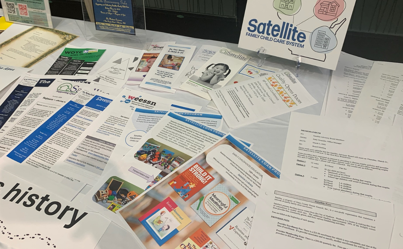 A table with various brochures, flyers, and documents about Satellite Family Child Care System programs and services.