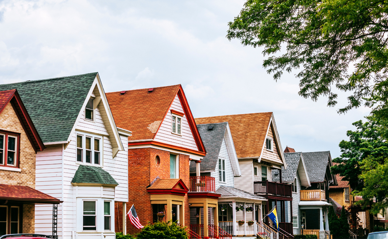 Row of colorful, gable-roofed houses with porches and American flags under partly cloudy sky.