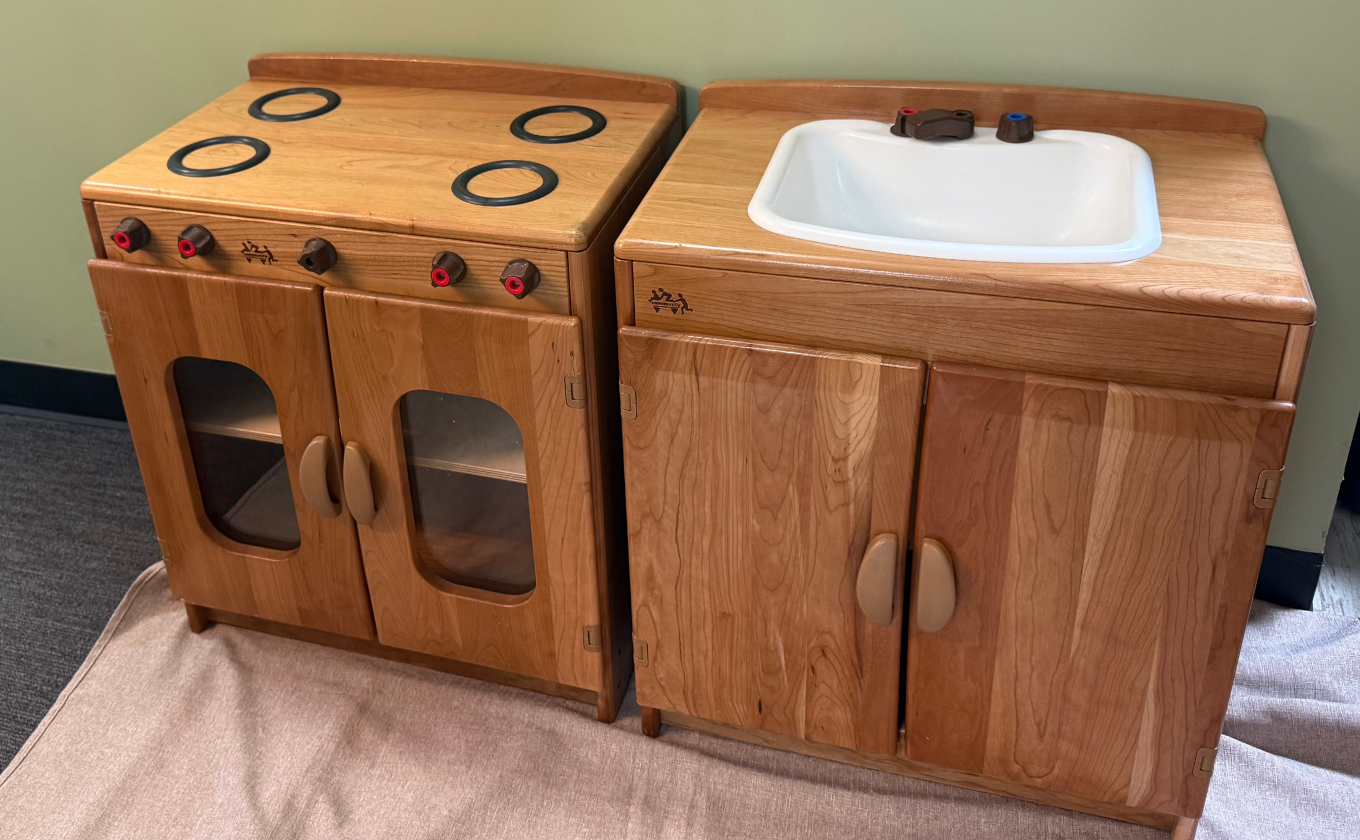 Wooden toy kitchen set with stove featuring four burners and a sink with red and blue knobs.