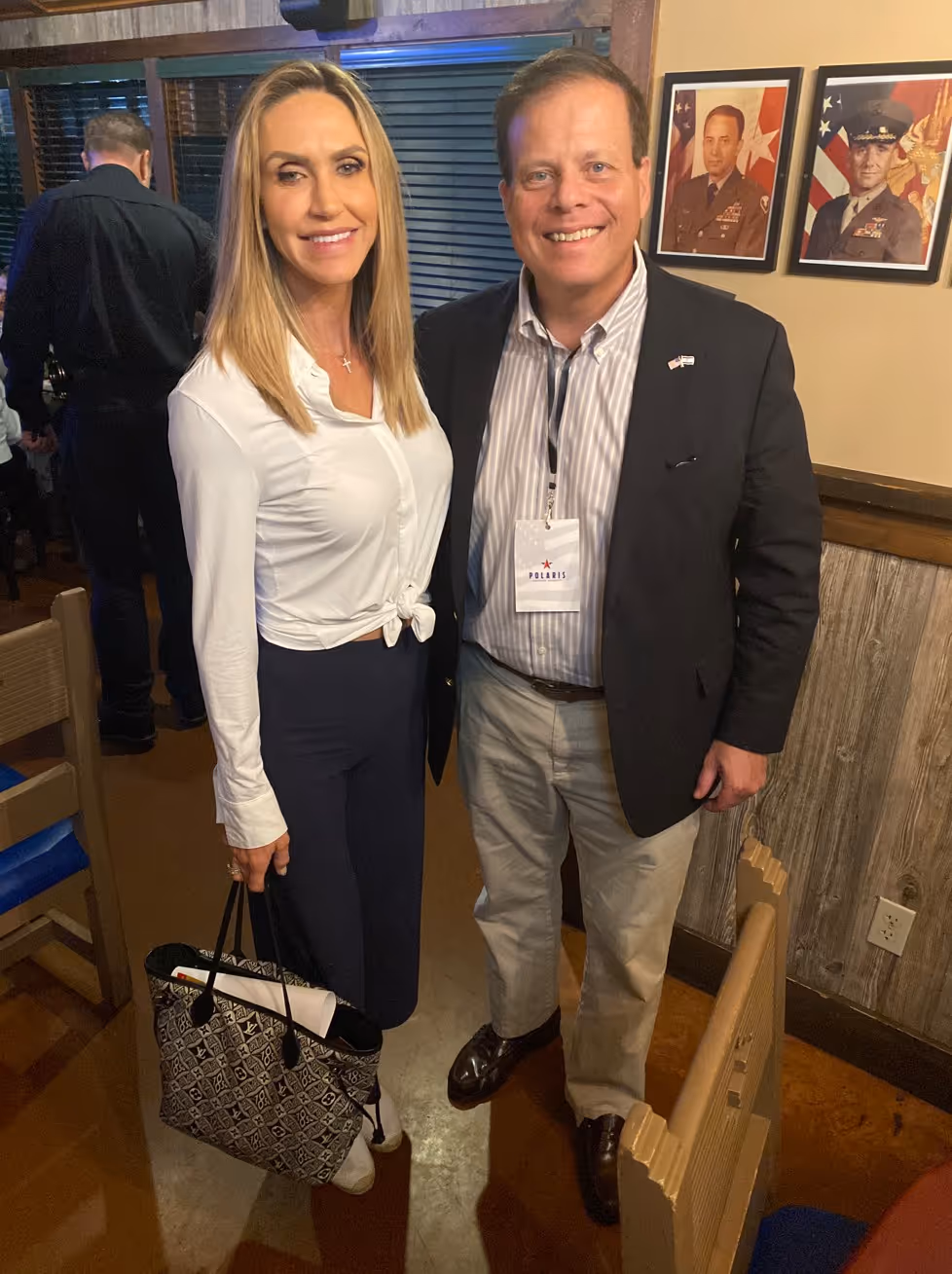 Smiling man in a striped shirt, blazer, and badge standing next to a woman in a white blouse.