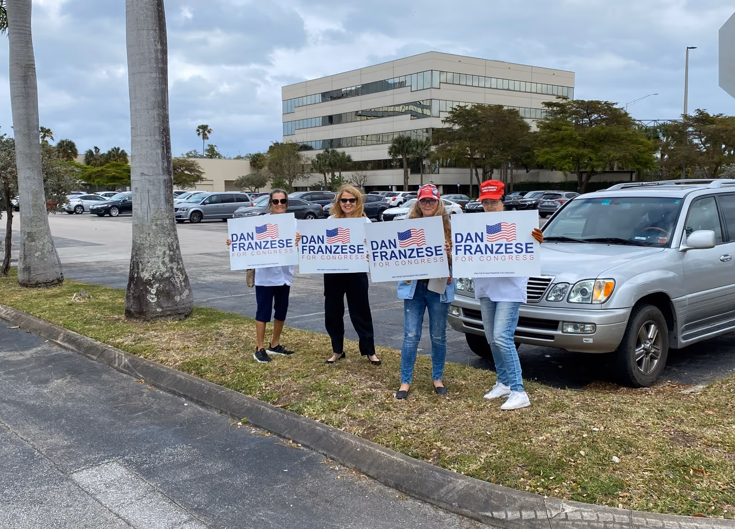 Four women standing on grass by a parking lot holding signs that say 'Dan Franzese for Congress' with an American flag graphic.