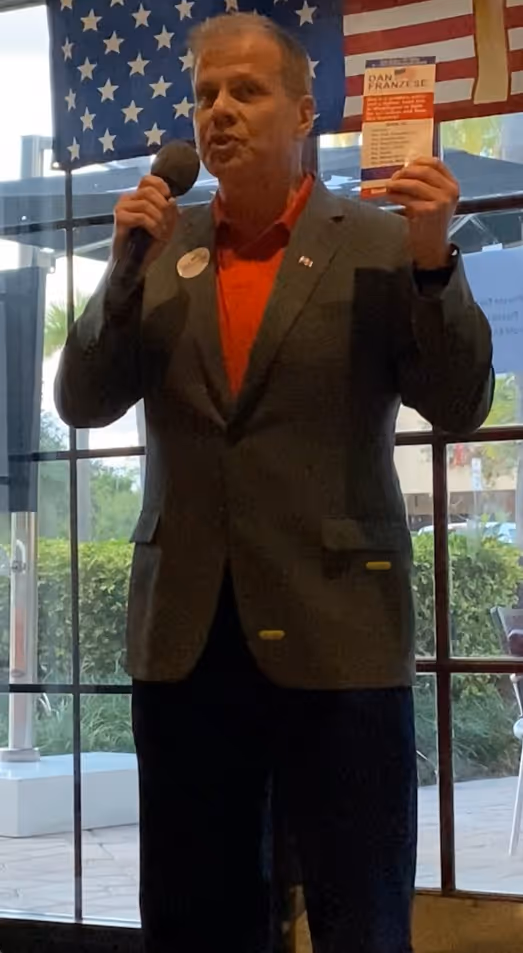 Man in a blazer and red shirt speaking into a microphone.