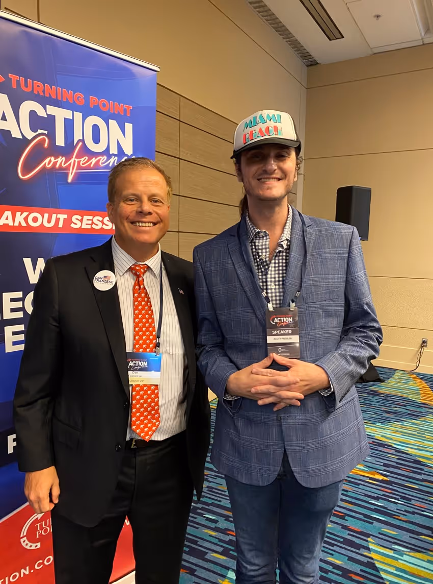 Two men smiling indoors at a conference.