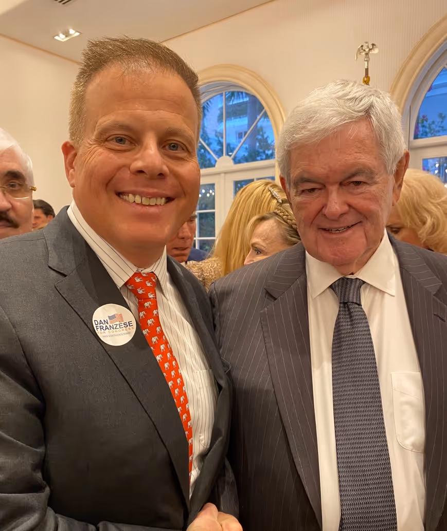 Two men in suits smiling at an indoor event.