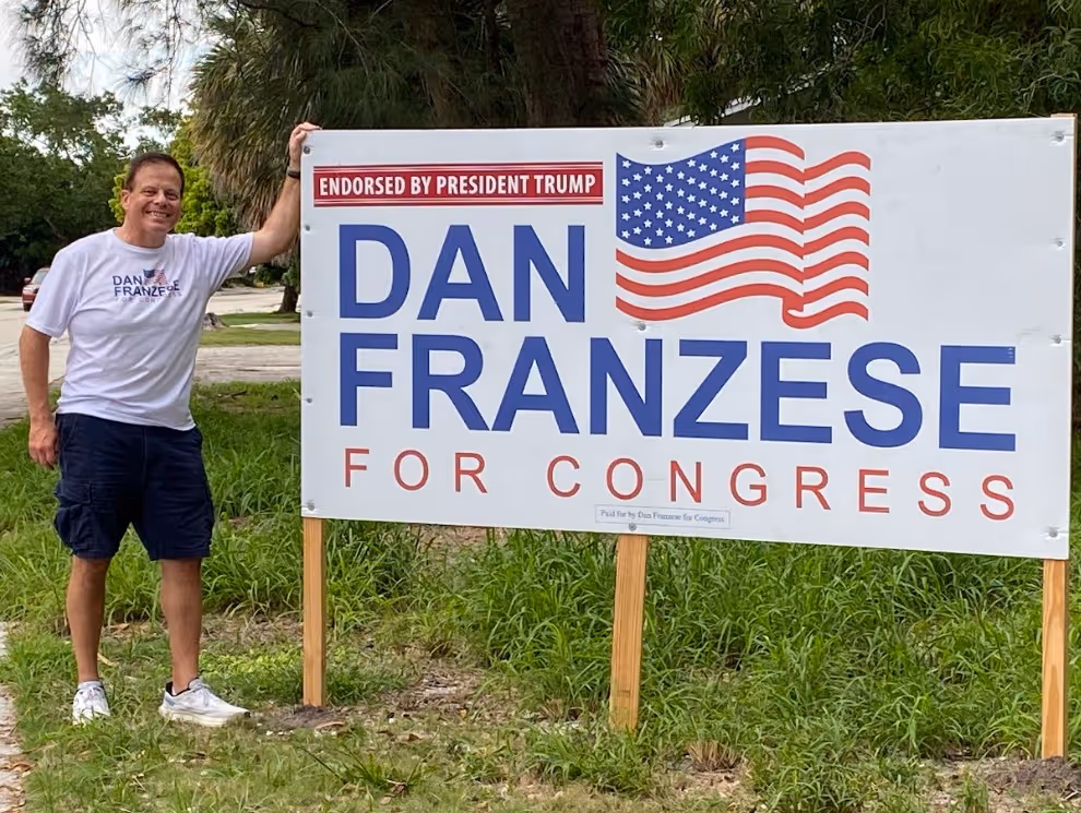 Two people smiling outdoors wearing Dan Franzese for Congress t-shirts and holding campaign flyers.