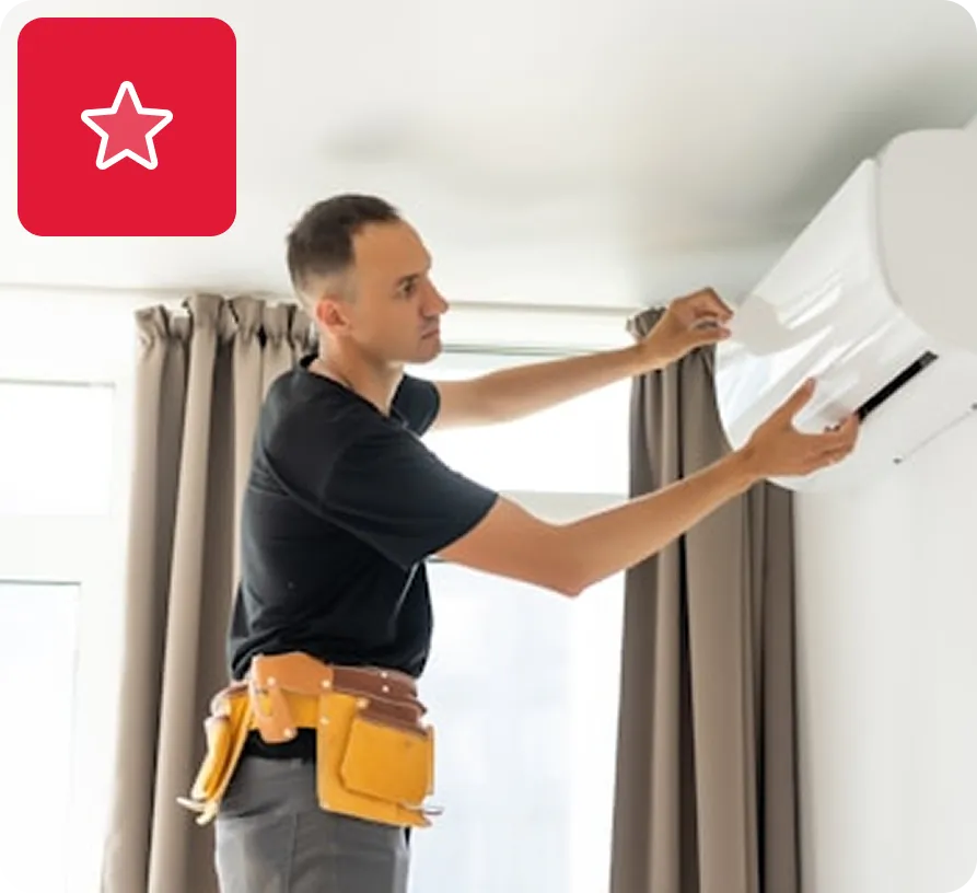 Technician installing or repairing a wall-mounted air conditioning unit inside a room.