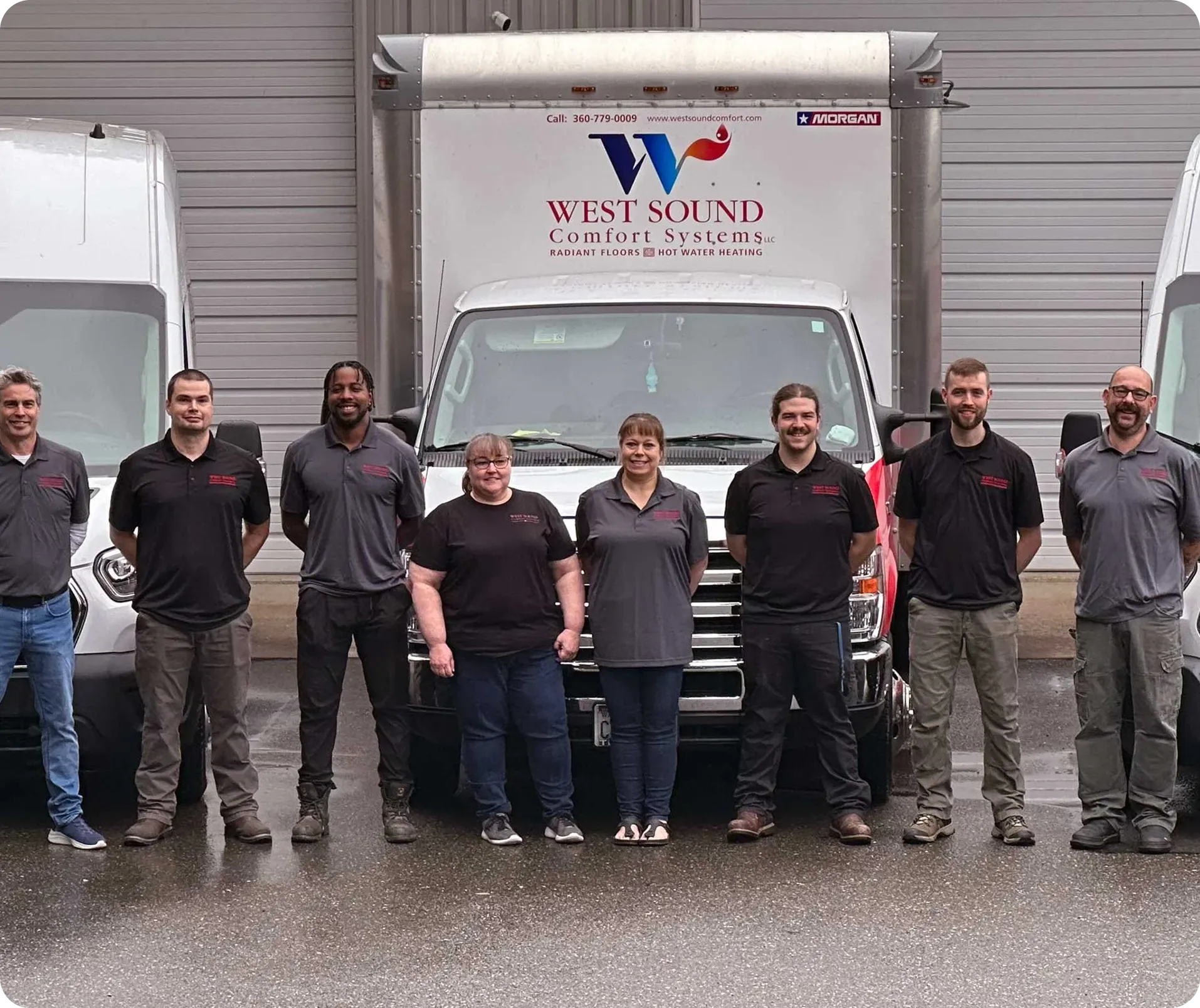 Eight employees standing in front of three company vans with West Sound Comfort Systems logo visible on the central van.