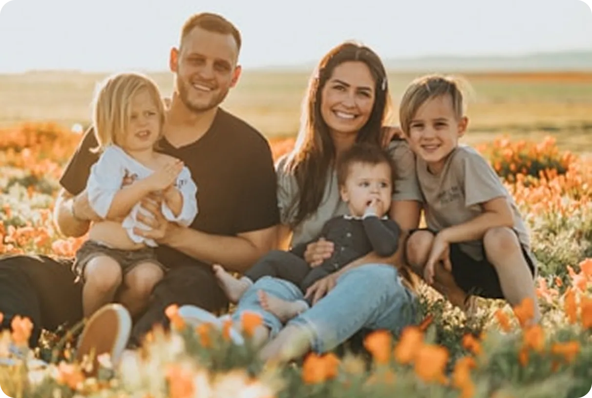 A smiling family of five sitting in a field of orange and white flowers during golden hour.