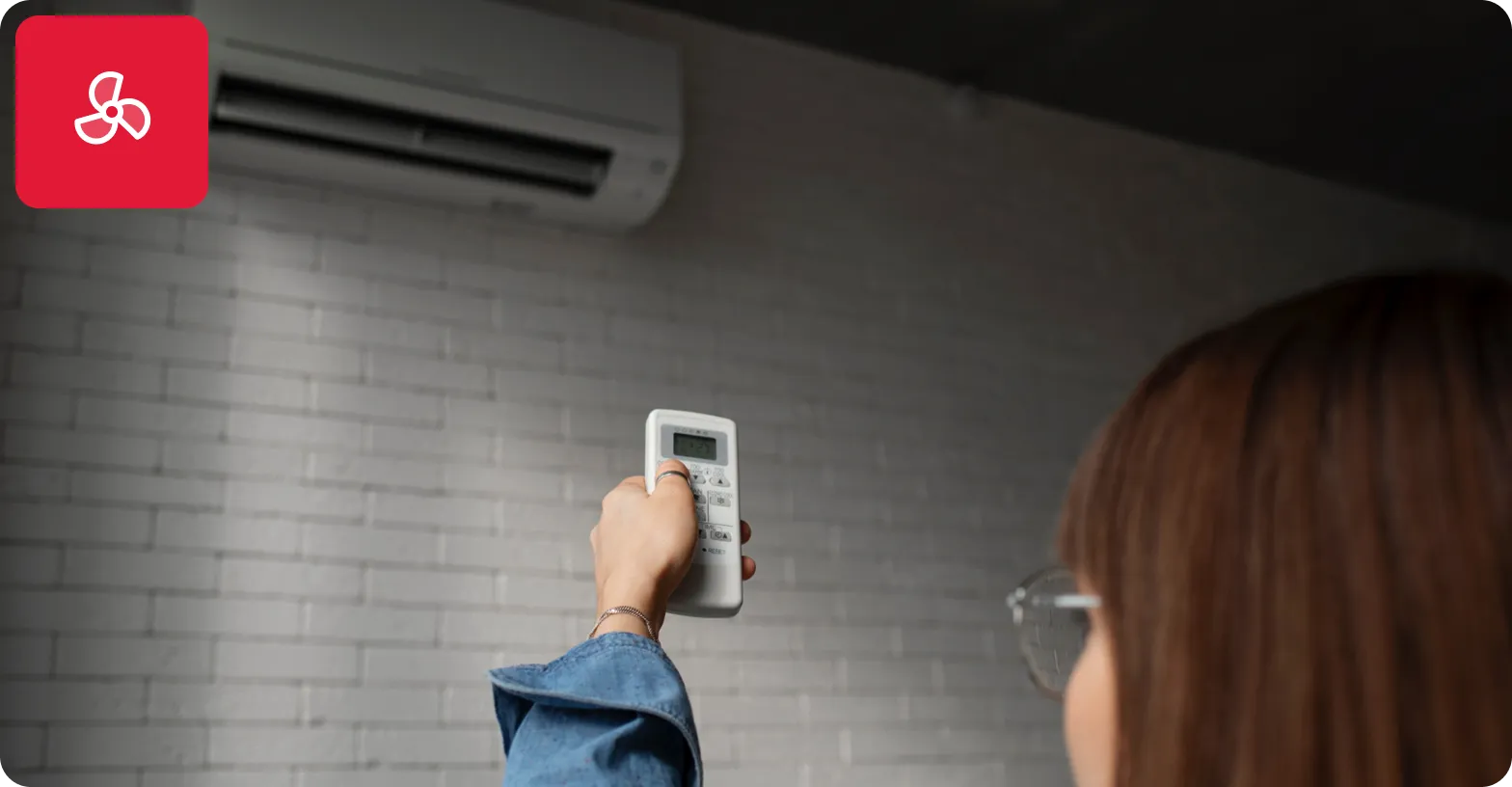 Person holding a remote control pointing at a wall-mounted air conditioner.