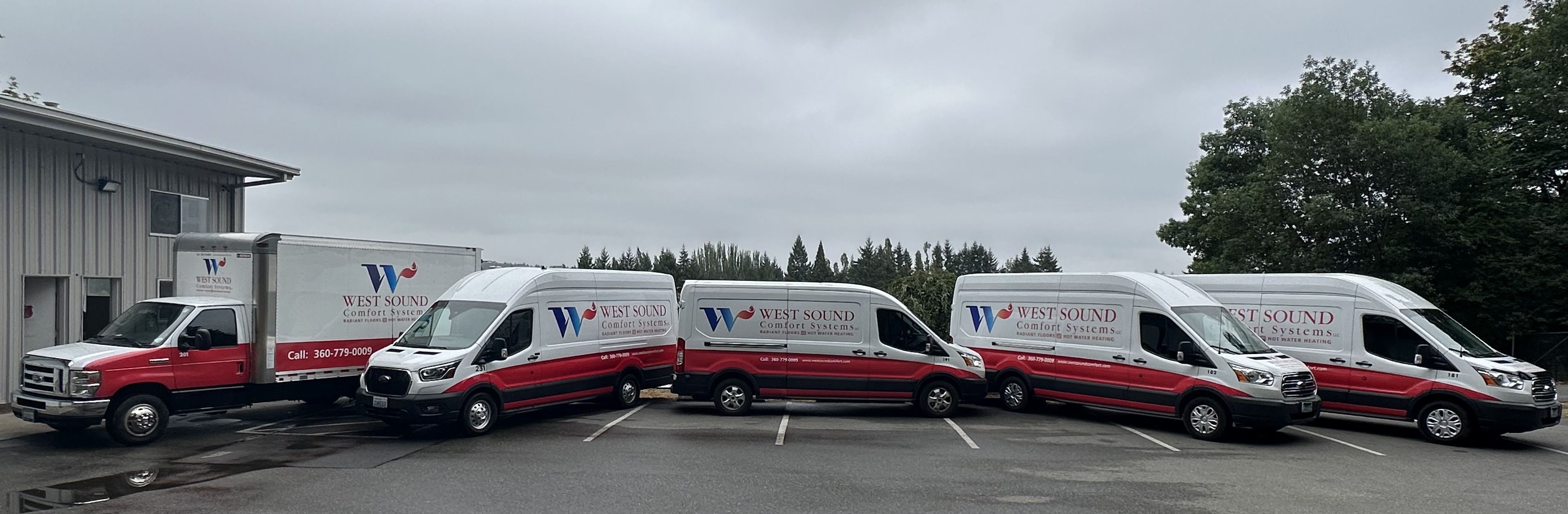 Five West Sound Comfort Systems company vans and a truck parked in a row outside a gray building on a cloudy day.