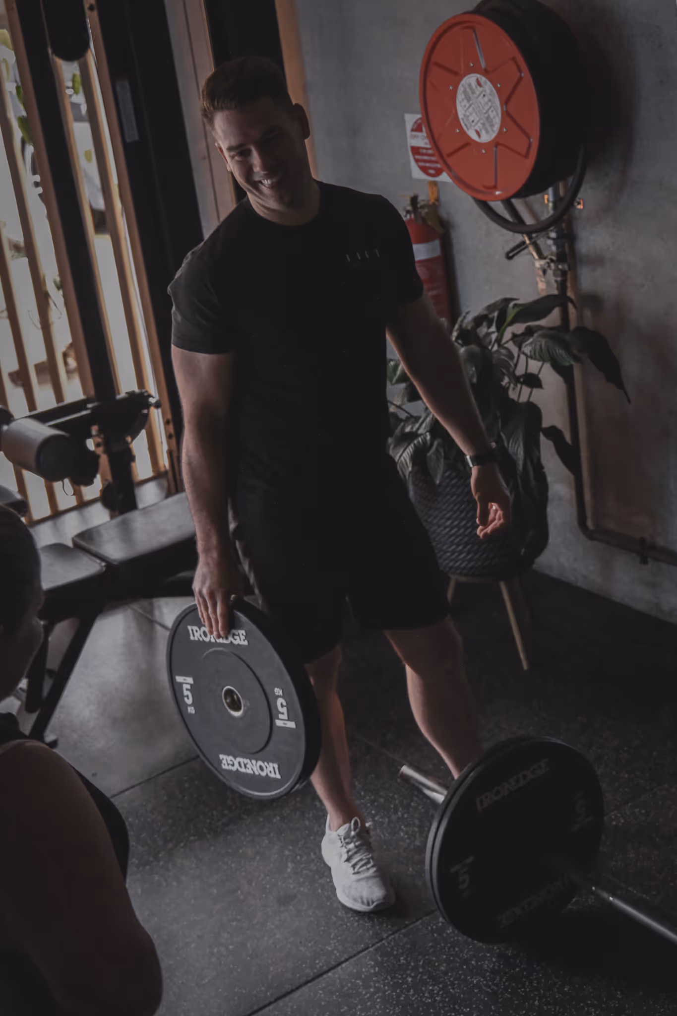 Man in black athletic wear holding a 5 kg weight plate in a gym setting.