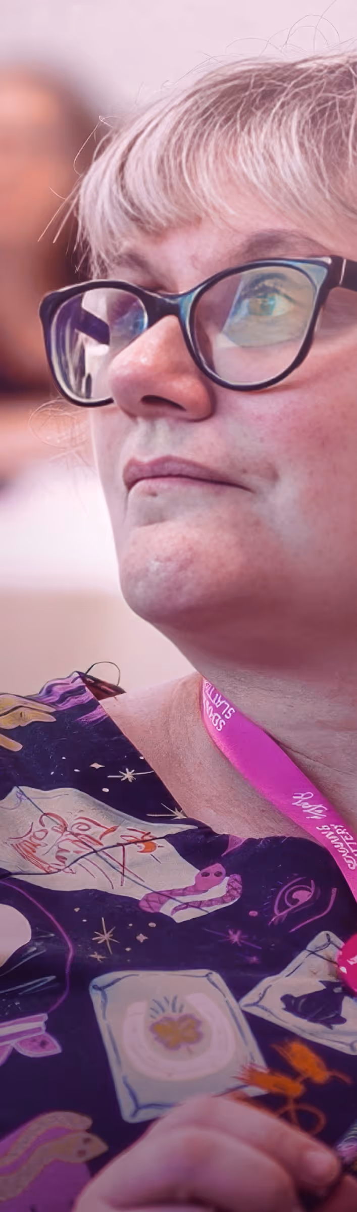 Close-up of a woman wearing glasses and a patterned shirt, looking thoughtfully to the side.