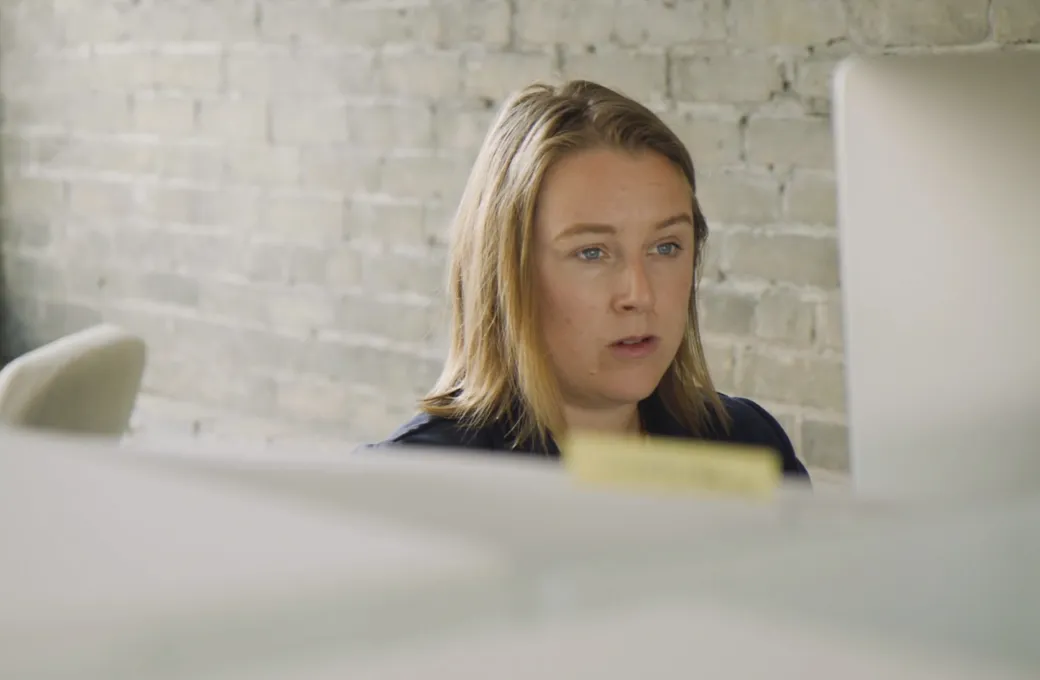 A woman with brown hair and a blue shirt looking at a computer.
