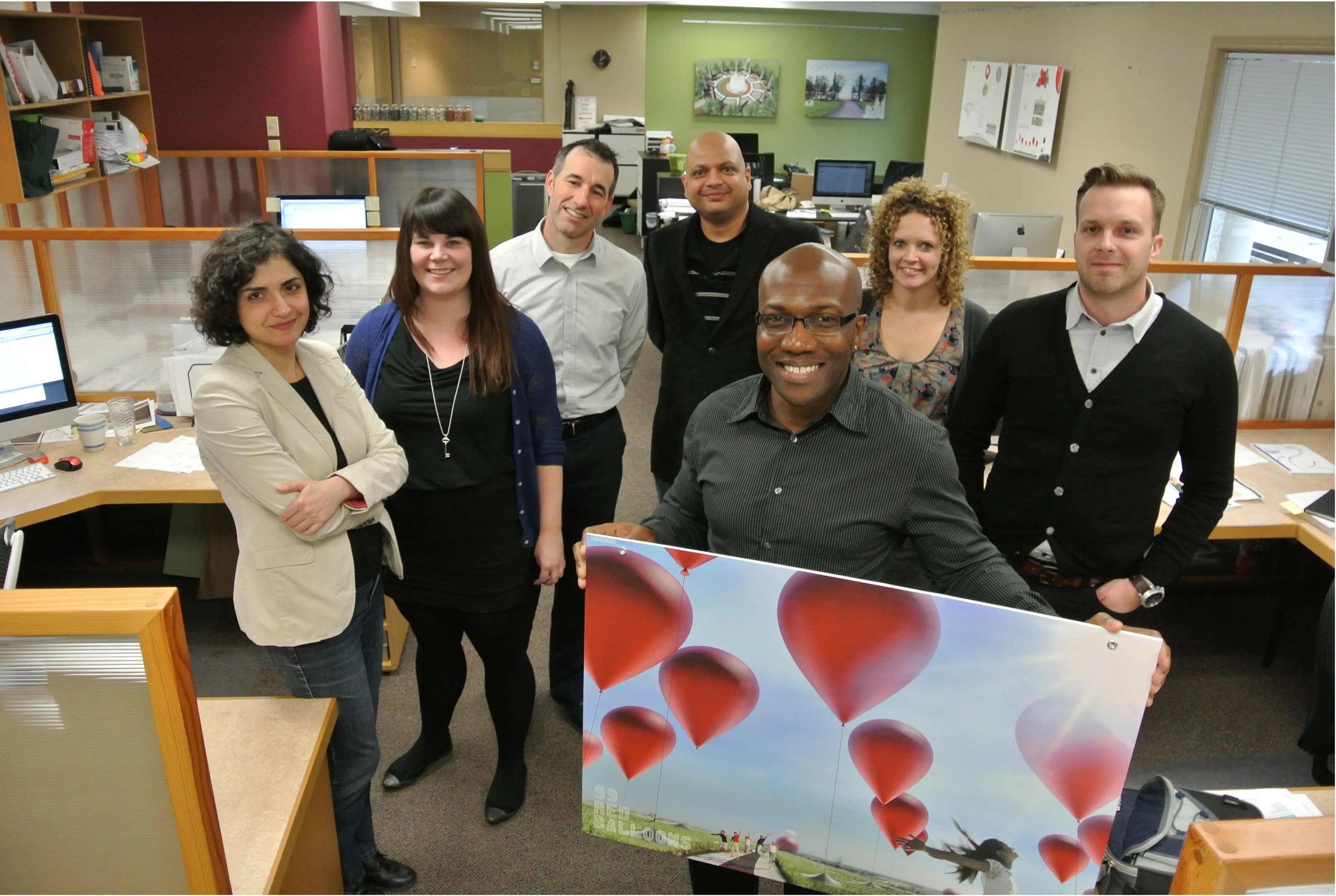 A group of people standing in front of a painting of red balloons.