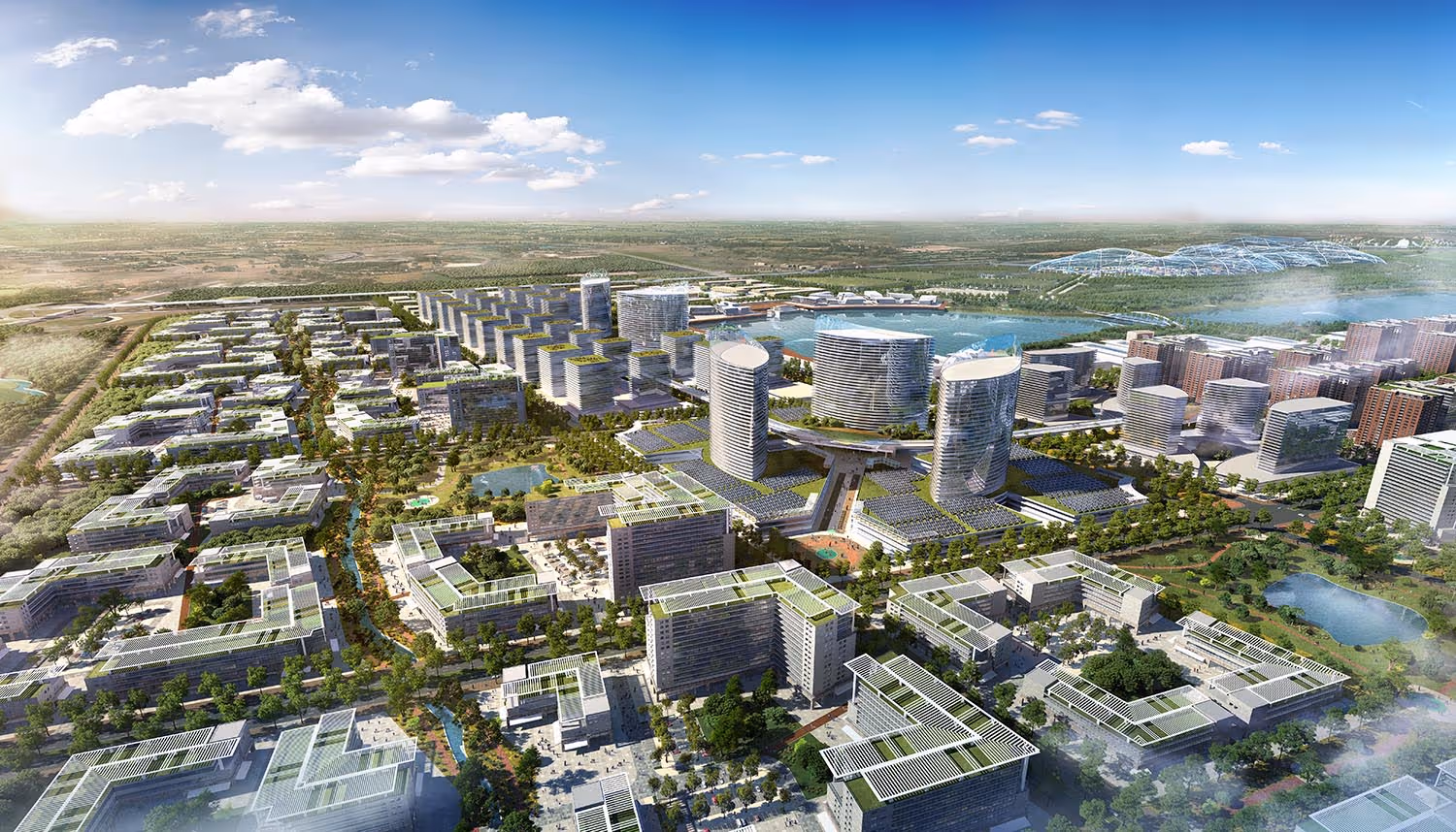 Aerial view of a modern mixed-use urban development with high-rise towers, green rooftops, waterways, and landscaped parks under a partly cloudy sky.