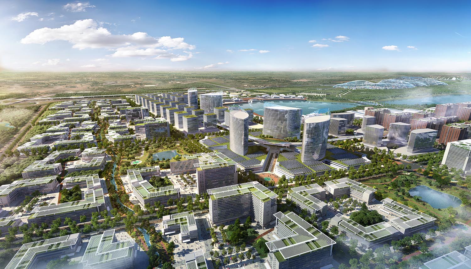 Aerial view of a modern mixed-use urban development with high-rise towers, green rooftops, waterways, and landscaped parks under a partly cloudy sky.