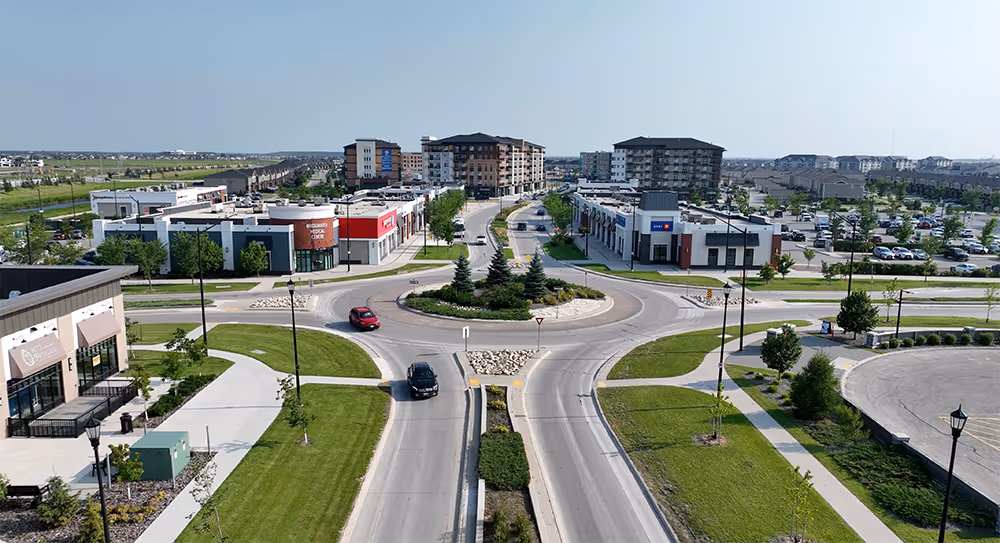 Aerial view of a modern roundabout with landscaped center surrounded by commercial buildings and parking lots in a suburban area.