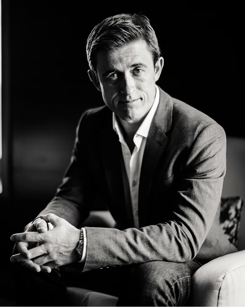 Black and white portrait of a Scott Walker sitting on a chair with hands clasped, looking at the camera.