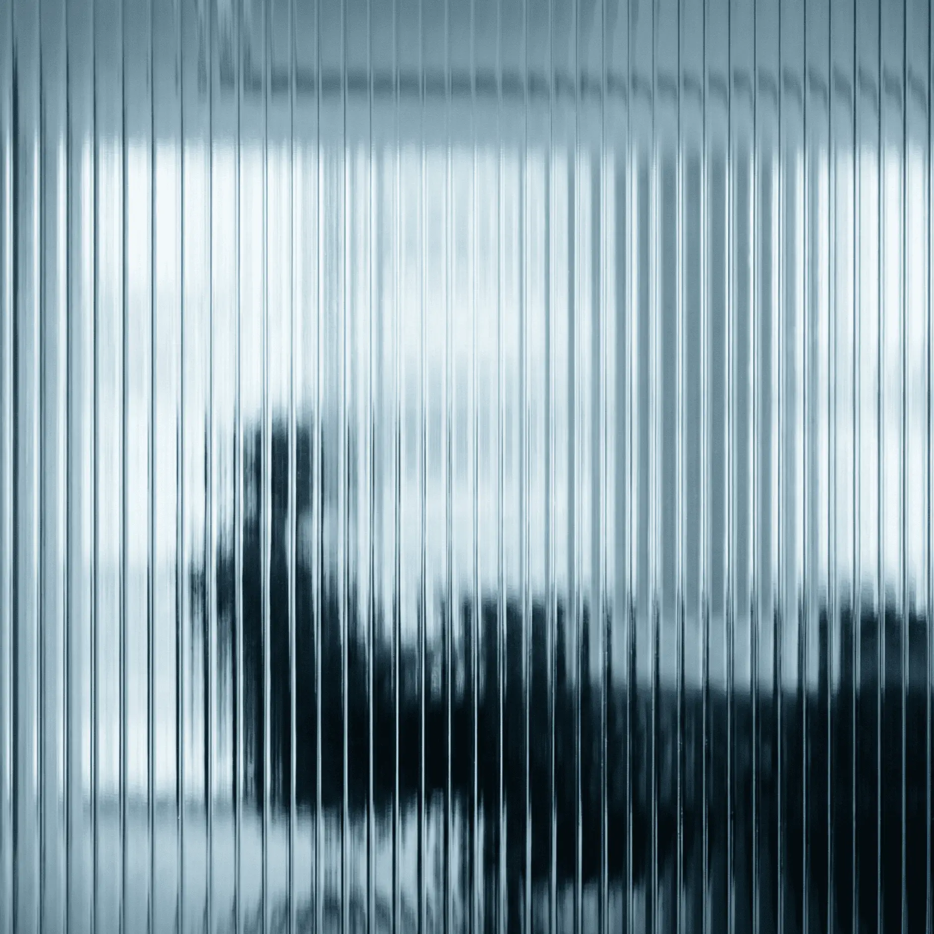 Blurred silhouette of a person sitting behind a vertically ribbed translucent glass wall.
