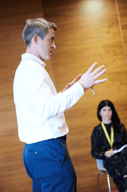 Scott Walker gesturing with hands while speaking, woman seated with notebook in background.