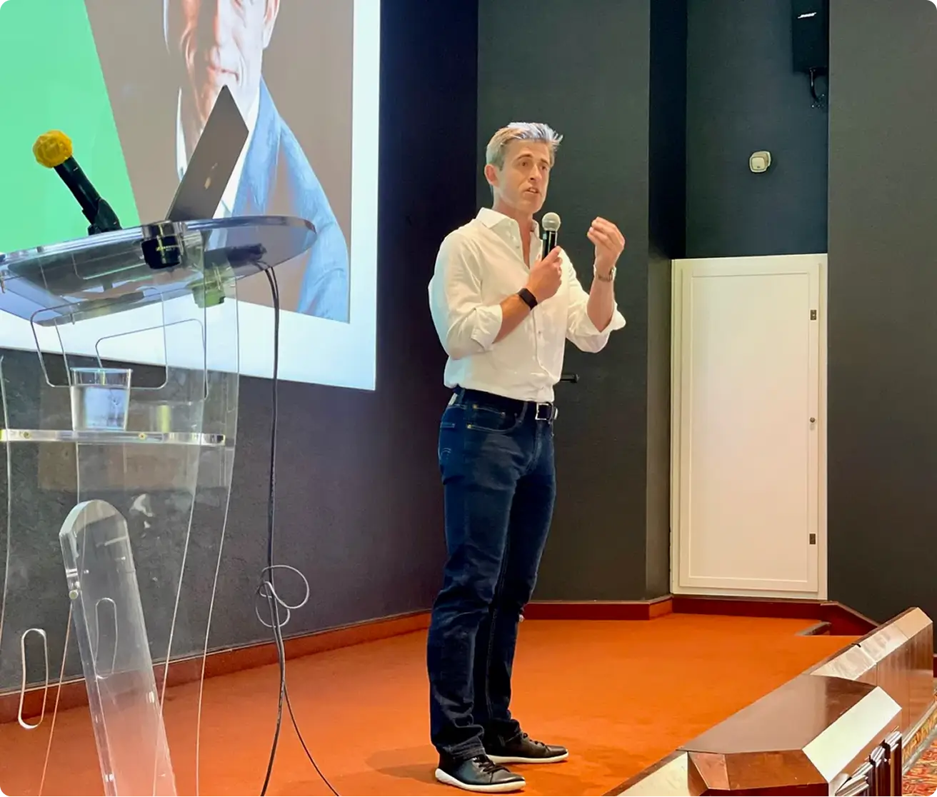 Scott Walker speaking into a microphone on stage with a presentation screen behind him.