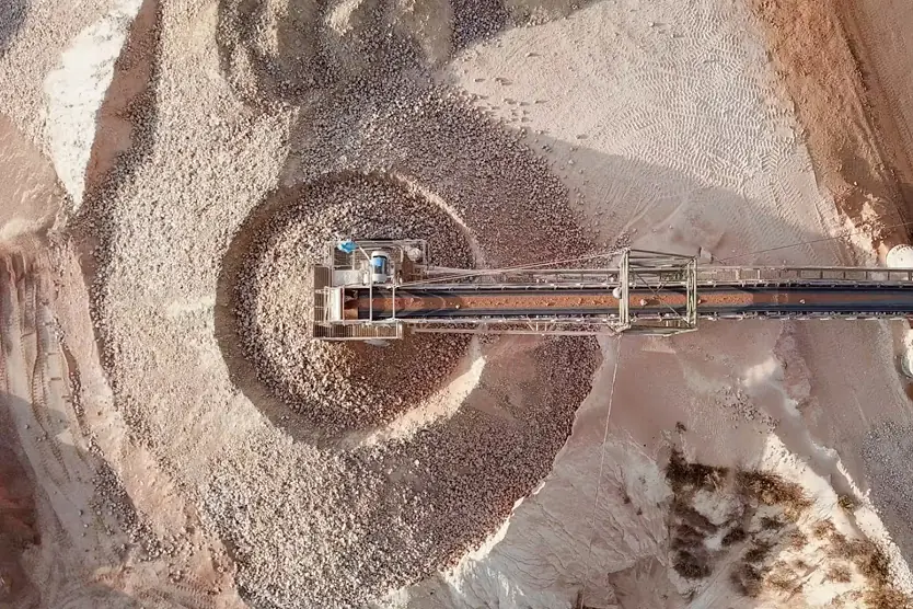 Vista aérea de una cinta transportadora apilando grava o rocas en montones circulares en un sitio de trabajo minero o de construcción.