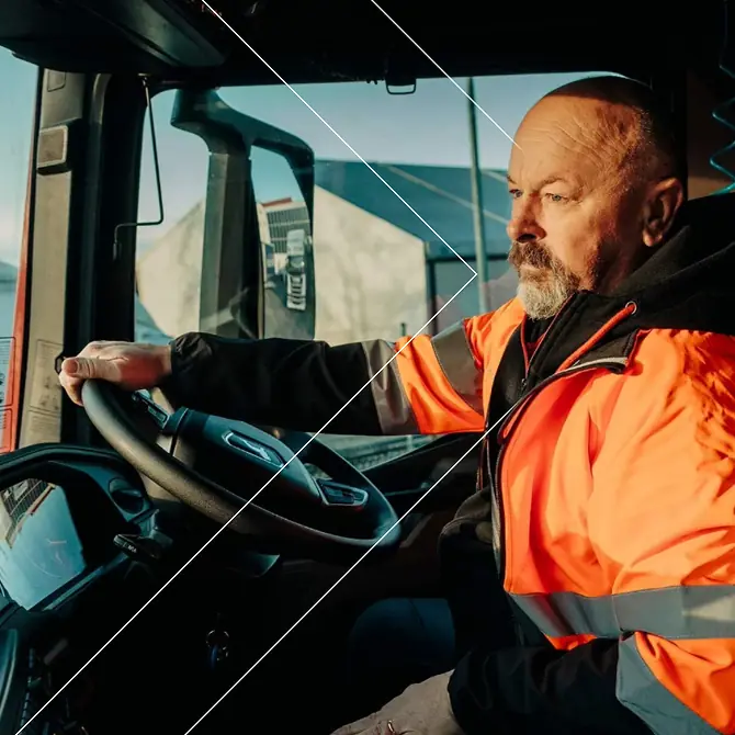Hombre de mediana edad con una chaqueta reflectante naranja conduciendo un camión, concentrado en la carretera.