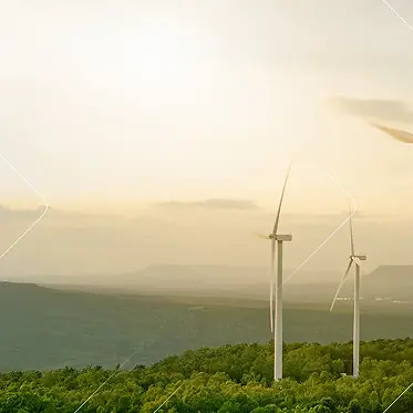 Dos aerogeneradores en una colina verde con un cielo brumoso y montañas lejanas al fondo.